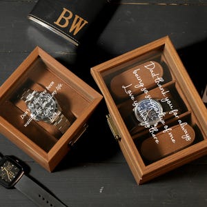 May include: Two wooden watch display boxes with glass lids, each holding a wristwatch. One box has the text "Don't be late. I've been waiting for you all my life. Love, Dick." The other box has the text "Dad, thank you for always being so supportive of me. Love is always there."