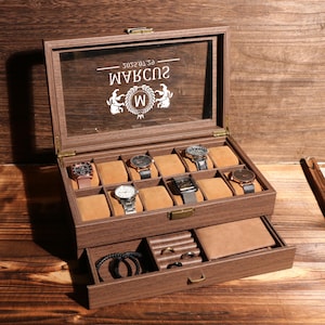 May include: A wooden watch box with a glass top, displaying several watches on tan cushions. The box has a drawer with space for jewelry and accessories. The glass top has the text "W" and other text.