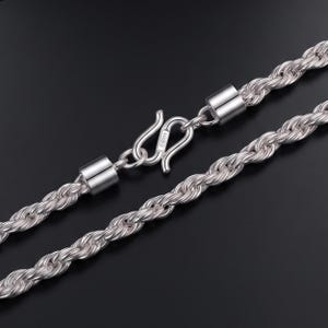 May include: A silver rope chain necklace featuring a polished finish and a secure S-hook clasp. The clasp is engraved with the text 足银999, indicating the purity of the silver. The chain consists of twisted metal links that create a textured appearance.