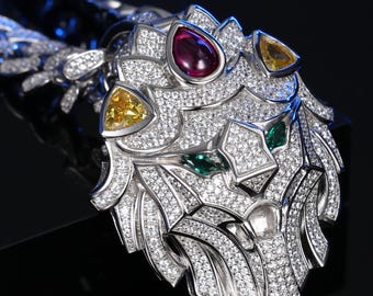 May include: A silver lion pendant necklace with a detailed design. The lion's head is encrusted with small, clear gemstones and features a ruby, yellow, and emerald-colored gemstones. The necklace has a matching silver chain.