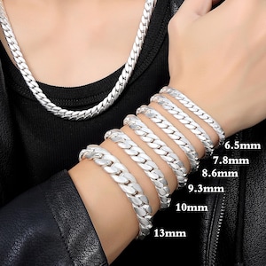 May include: A collection of silver-colored chain bracelets in various widths, ranging from 6.5mm to 13mm, displayed on a wrist. A matching chain necklace is also visible. The jewelry is shown against a black background.
