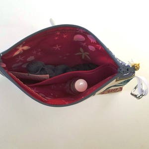 May include: A blue and white patterned zippered pouch with a red lining. The pouch is open and contains a small pink and white roll-on bottle and a small piece of fabric.