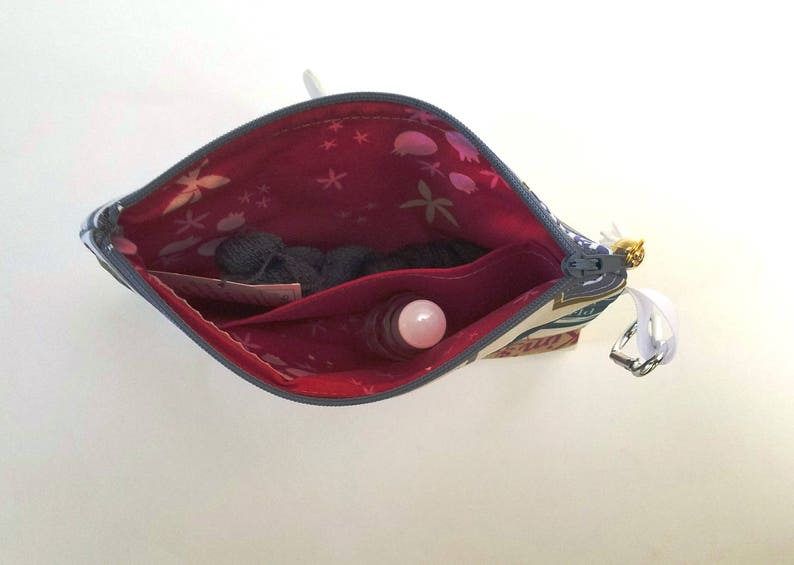 May include: A blue and white patterned zippered pouch with a red lining. The pouch is open and contains a small pink and white roll-on bottle and a small piece of fabric.