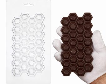 May include: A clear plastic rectangular mold featuring a repeating hexagonal honeycomb pattern, alongside a dark brown chocolate bar cast in the same hexagonal shape, displaying a textured surface within each individual hexagon cell.