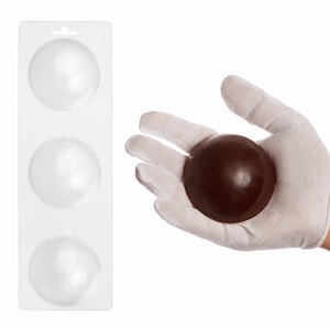 May include: A clear plastic mold tray featuring three circular cavities for shaping spheres, positioned alongside a single dark brown spherical object held in a white fabric glove, showcasing the finished product shape and size.
