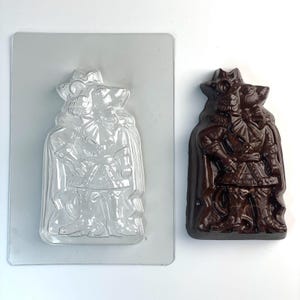 Puede incluir: Un molde de plástico transparente y una figura de chocolate negro. El molde tiene la forma de una persona con sombrero y capa. La figura de chocolate es una réplica detallada del molde, con detalles de ropa visibles.