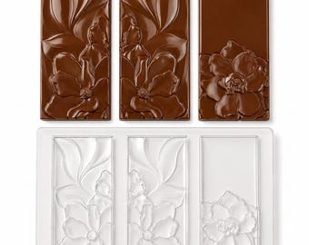 May include: A clear rectangular plastic mold with three distinct cavities featuring embossed floral and leaf patterns, accompanied by three molded brown chocolate bars that mirror the intricate botanical designs of the mold's interior.