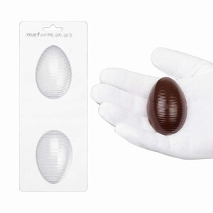 May include: A clear plastic mold with two oval cavities featuring horizontal ribbed textures, accompanied by a single dark brown chocolate egg with matching horizontal ribbed details, held in a white gloved palm.