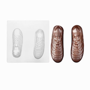 May include: A clear plastic mold with two football cleat impressions and two brown chocolate cleats. The cleats have laces and a textured design. The mold is on a white background.