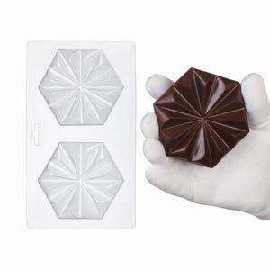 Può includere: Uno stampo in plastica trasparente con due cavità esagonali caratterizzate da un design floreale a petali multipli in rilievo, accanto a un singolo pezzo di cioccolato esagonale marrone scuro che riproduce il motivo geometrico a stella.