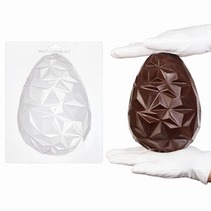 Può includere: Uno stampo a forma di uovo geometrico in plastica trasparente con un design a facce e un uovo di cioccolato marrone scuro con lo stesso motivo geometrico sfaccettato. Lo stampo ha un supporto rettangolare con un piccolo foro in alto.