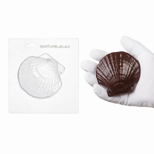 Può includere: Un oggetto a forma di conchiglia, marrone scuro, tenuto in una mano guantata, accanto a una carta bianca con un contorno di conchiglia e il testo "murforma.in.ua". La conchiglia presenta creste dettagliate e una superficie strutturata.