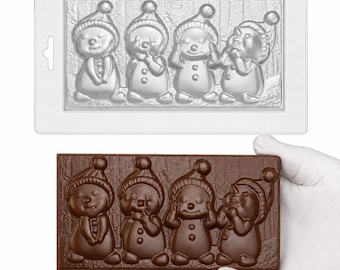 May include: A rectangular clear plastic mold featuring four distinct snowman figures in winter hats, positioned side-by-side against a textured wood-grain background, accompanied by a matching dark brown chocolate bar cast from the same mold.