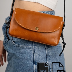 Könnte beinhalten: Eine hellbraune Umhängetasche aus Leder mit abgerundeter Klappe, einem einzelnen messingfarbenen Druckknopfverschluss und dünnen schwarzen Kordelriemen. Die Tasche hat sichtbare weiße Nähte an der Klappenkante und trägt den Schriftzug FONDER Atelier.