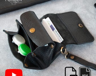 May include: Black leather wallet with multiple compartments, including one for contact lenses and another for cash. The wallet has a wrist strap and a snap closure. The word "FONDER" is visible in the upper left corner.