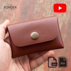 Könnte beinhalten: Eine braune Ledergeldbörse mit Klappenverschluss und einem Metallknopf. Die Geldbörse wird in einer Hand gehalten. Das Wort "FONDER Atelier" befindet sich in der oberen linken Ecke. Ein YouTube-Logo und SVG/PDF-Symbole befinden sich im Bild.