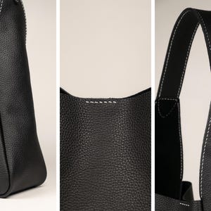 May include: Close-up shots of a black leather tote bag with white stitching. The bag has a textured surface and a simple, modern design. The stitching is visible along the seams and handles, adding a contrasting detail.