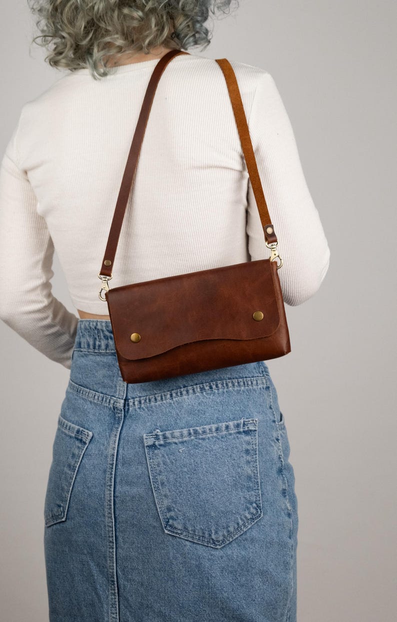 Peut inclure: Un sac bandouli&egrave;re en cuir marron avec une fermeture &agrave; rabat et deux boutons dor&eacute;s. Le sac est dot&eacute; d'une longue bandouli&egrave;re r&eacute;glable. Le sac est port&eacute; &agrave; l'&eacute;paule.