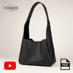 Op de afbeelding: Zwarte leren schoudertas met een afgeronde bodem en een enkele handgreep. De tas heeft witte stiksels langs de naden en handgreep. De merknaam "FONDER Atelier" is zichtbaar in de linkerbovenhoek.