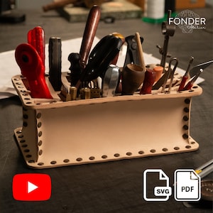 May include: A light tan leather tool organizer filled with various tools. The organizer is rectangular with brass rivets and a slotted top. Tools include screwdrivers, pliers, and other craft tools. The logo "FONDER Atelier" is visible.