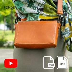 May include: A tan leather crossbody bag with a rectangular shape and a long, adjustable strap. The bag has a front flap and visible stitching. The words "FONDER Atelier" are visible. The bag is worn over the shoulder.