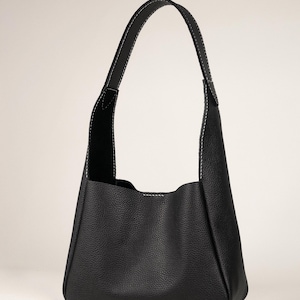 May include: A black leather shoulder bag with a rounded bottom and a single handle. The bag features white stitching along the seams and handle, and has a textured surface.