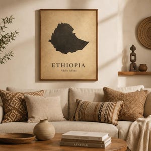 May include: A rectangular framed wall art print featuring a black silhouette map of Ethiopia centred on a textured, light brown parchment-style background. The text ETHIOPIA is printed in black capital letters above the text Addis Ababa.
