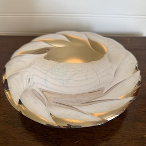 May include: A decorative glass bowl with a swirling design. The bowl features a gold-colored interior and a white and gold exterior. The bowl is round and has a textured, wavy pattern. The bowl is sitting on a dark wooden surface.