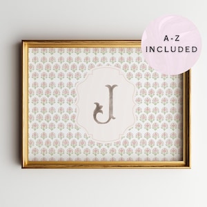 May include: A framed print featuring a floral pattern in pink and green. The print has a light pink background with a decorative letter "J" in the center. The text "A-Z INCLUDED" is in a pink circle in the upper right corner.