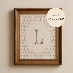 May include: A framed print with the letter "L" in a decorative font. The letter is centered on a light beige background within a patterned frame. The frame is a dark brown colour, and the print includes the text "A - Z INCLUDED".