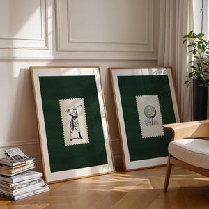 May include: Two framed art prints with golf illustrations. Each print has a dark green background with a postage stamp-style image in the centre. One shows a golfer swinging, the other a golf ball on a tee. The frames are light brown.