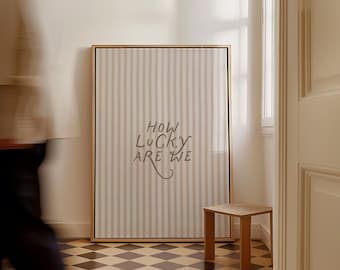May include: A framed artwork with vertical beige and white stripes and the text "HOW LUCKY ARE WE" in a modern font. A small wooden side table sits to the right of the artwork. The floor has a black and white checkered pattern.