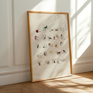 May include: A framed alphabet art print. The print features the letters of the alphabet, each accompanied by a corresponding illustration. The artwork is in a wooden frame and leans against a white wall. The illustrations are in various colors.