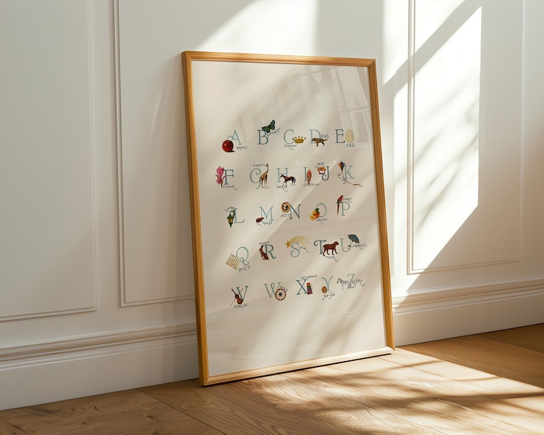 May include: A framed alphabet art print. The print features the letters of the alphabet, each accompanied by a corresponding illustration. The artwork is in a wooden frame and leans against a white wall. The illustrations are in various colors.