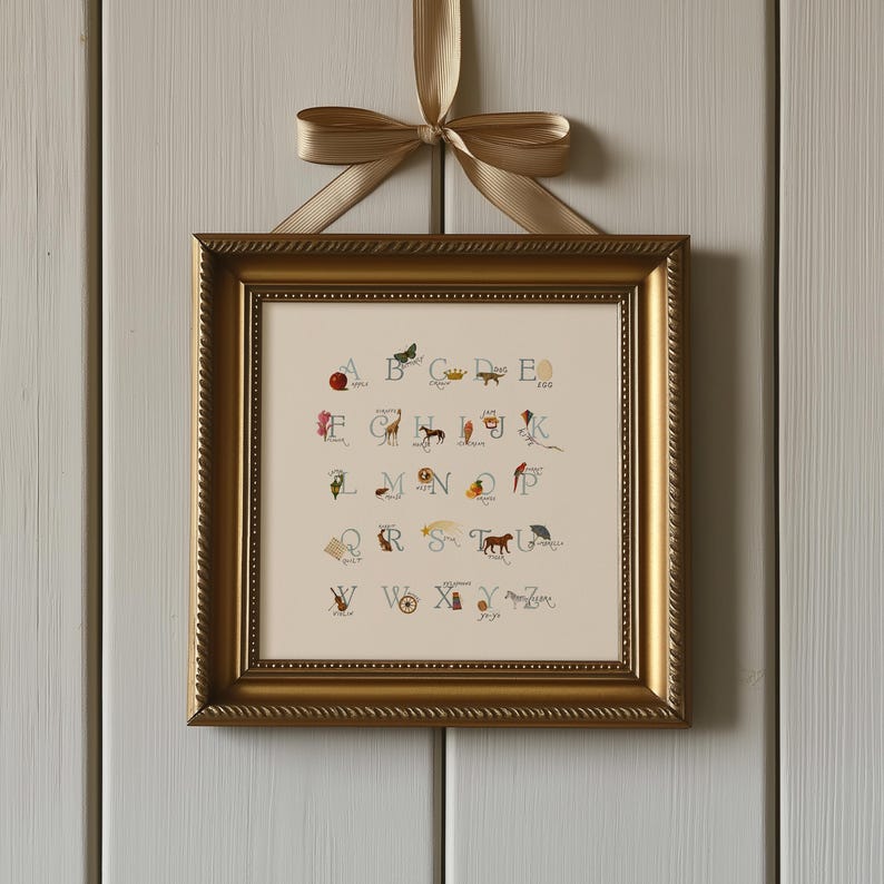 May include: A framed alphabet print with a gold-colored frame and a cream-colored background. Each letter is accompanied by a small illustration. The frame is suspended by a gold ribbon tied in a bow.
