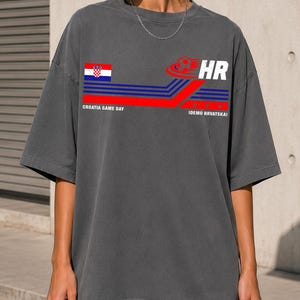 May include: A charcoal gray oversized t-shirt featuring a graphic print with the Croatian flag, a soccer ball icon, and the text "CROATIA GAME DAY" and "IDEMO HRVATSKA!" alongside blue and red horizontal stripes and the letters "HR" in white.