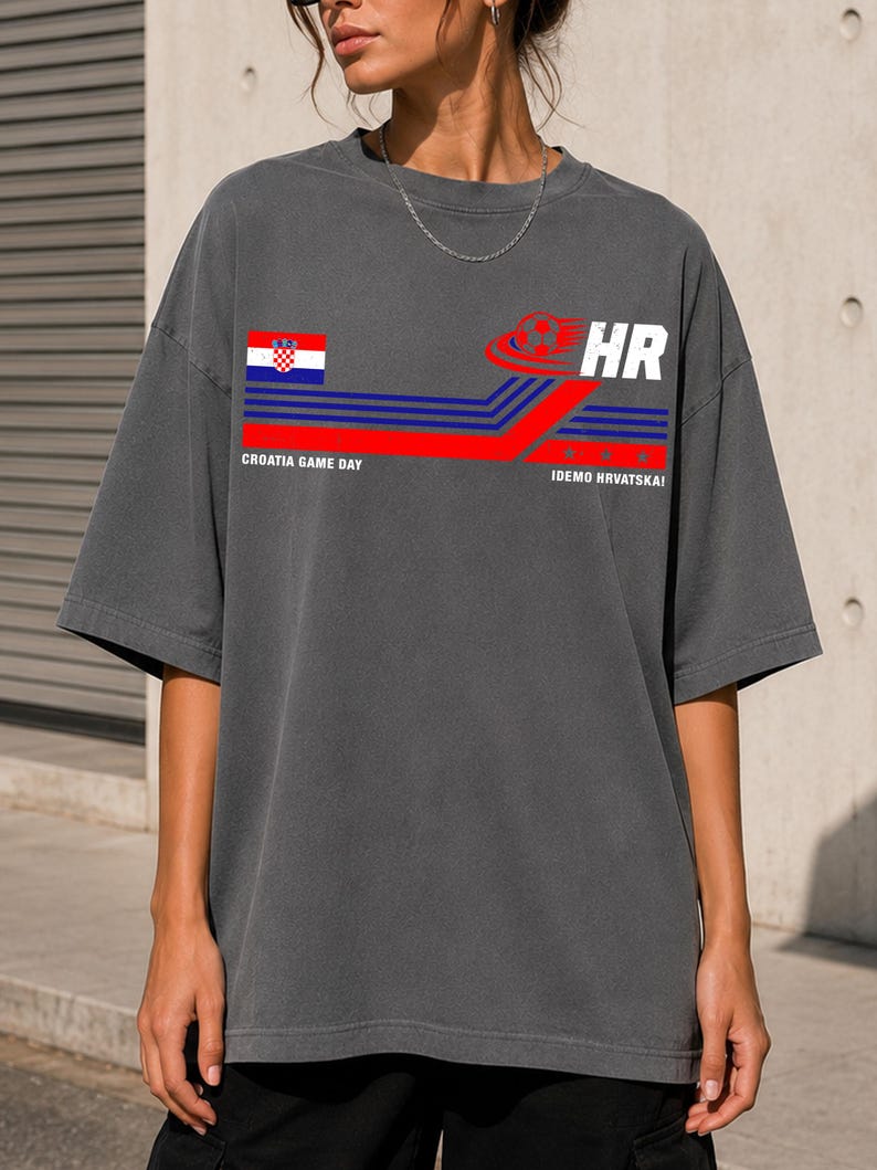 May include: A charcoal gray oversized t-shirt featuring a graphic print with the Croatian flag, a soccer ball icon, and the text "CROATIA GAME DAY" and "IDEMO HRVATSKA!" alongside blue and red horizontal stripes and the letters "HR" in white.