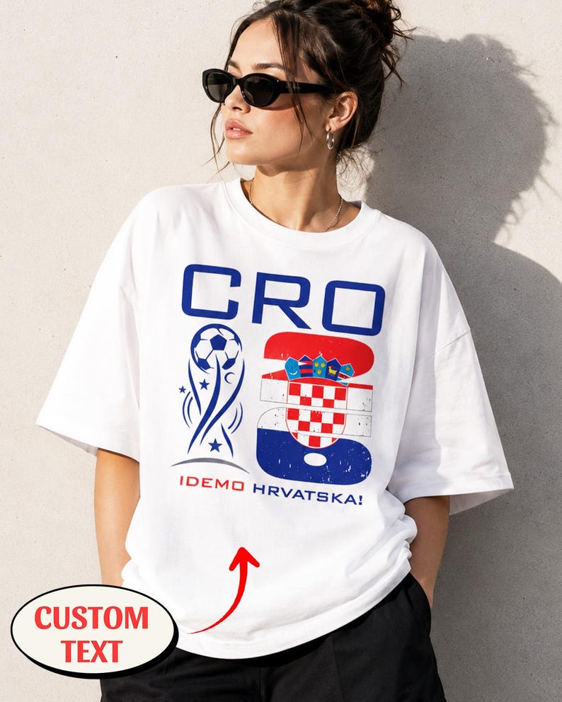 May include: A white short-sleeved t-shirt featuring a blue and red graphic design. The print includes the text CRO, a soccer ball icon, the number 26 with the Croatian flag pattern, and the text IDEMO HRVATSKA! in red and blue lettering.