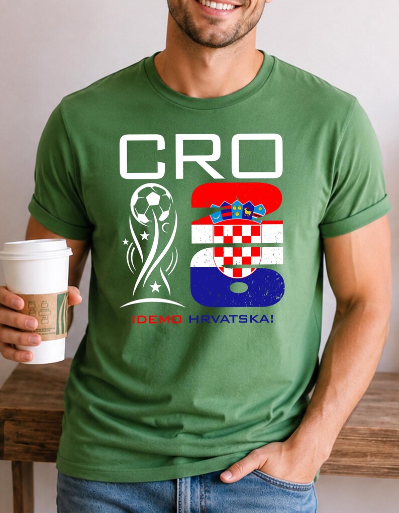May include: A sage green short-sleeve t-shirt featuring a white graphic with the text CRO 26. The design includes a soccer ball icon and the Croatian flag pattern within the number 26, with the text IDEMO HRVATSKA! printed in red and blue below.