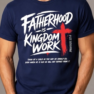 May include: A navy blue t-shirt featuring white text that reads "FATHERHOOD IS KINGDOM WORK" with a red cross graphic. Below the text, it reads "PROVERBS 22:6" and "TRAIN UP A CHILD IN THE WAY HE SHOULD GO; EVEN WHEN HE IS OLD HE WILL NOT DEPART FROM IT."