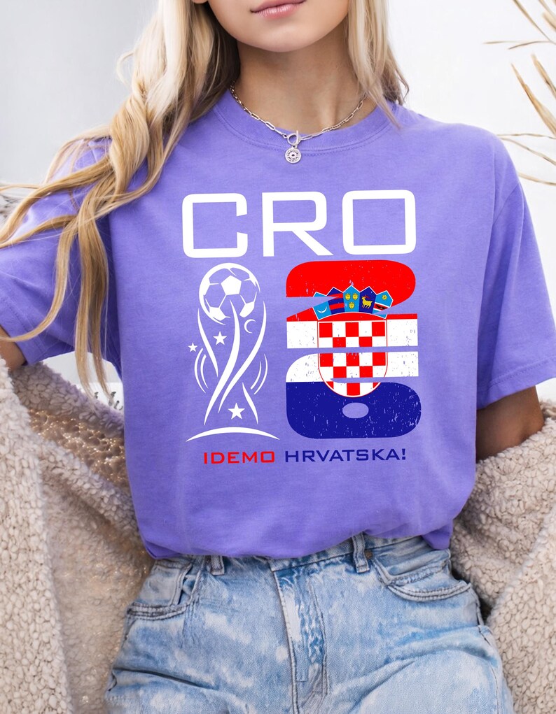 May include: A purple short-sleeve t-shirt featuring the white text CRO and the number 26. The number 26 is filled with the Croatian flag pattern. A white soccer ball graphic and the red and white text IDEMO HRVATSKA! are printed below.