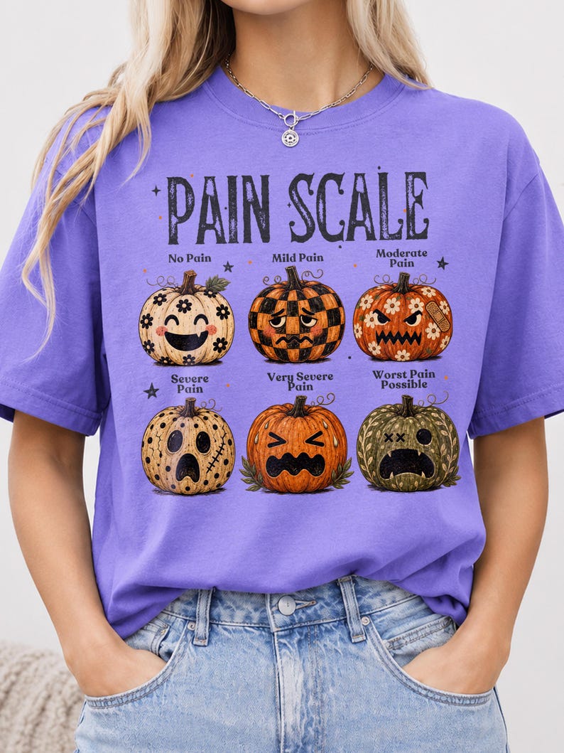 May include: A purple t-shirt featuring a graphic of six pumpkins arranged in two rows, labeled PAIN SCALE. Each pumpkin displays a different facial expression and pattern, representing levels from No Pain to Worst Pain Possible, with text labels.