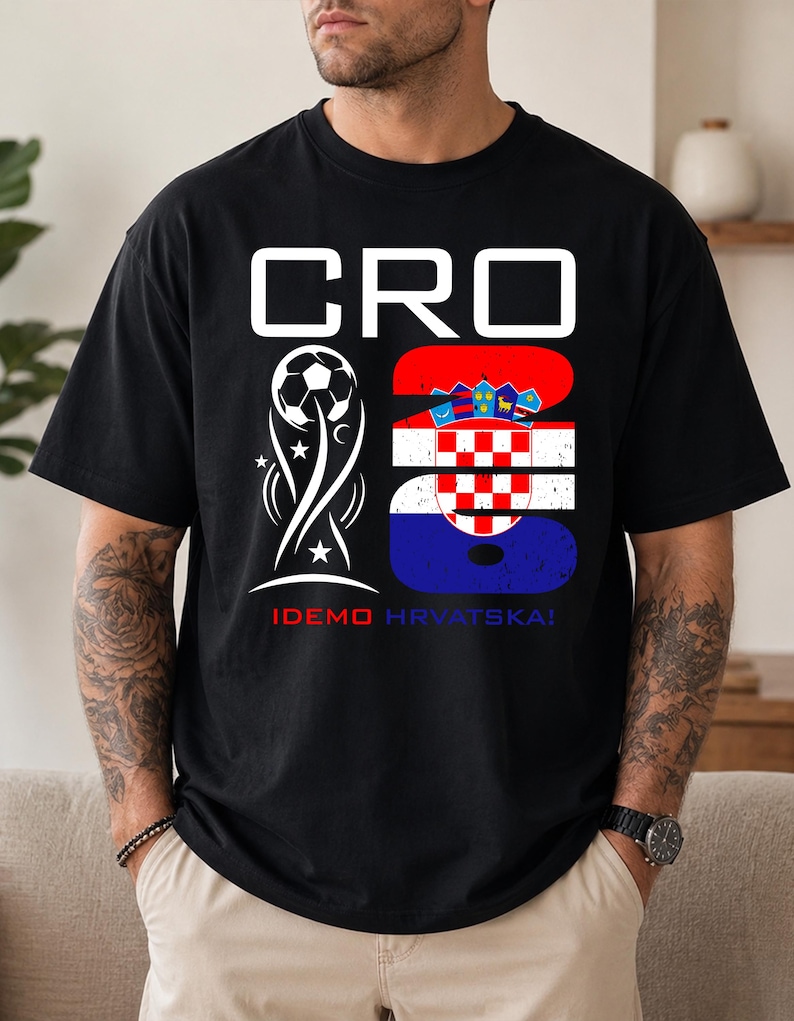 May include: A black t-shirt featuring a white graphic with the text CRO 26. The design includes a soccer ball trophy icon and the Croatian flag pattern within the number 26. Below the graphic, the text IDEMO HRVATSKA! is printed in red and blue.