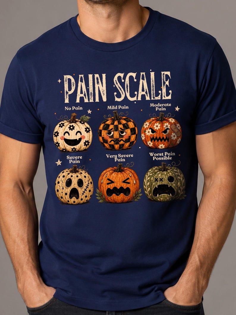 May include: A navy blue t-shirt featuring a graphic titled PAIN SCALE with six pumpkins showing different facial expressions. The pumpkins represent levels from No Pain to Worst Pain Possible, with various patterns, colors, and decorative elements.