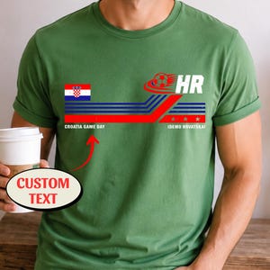 May include: An olive green t-shirt featuring a graphic with the Croatian flag, a soccer ball, and the text HR, CROATIA GAME DAY, and IDEMO HRVATSKA. A red arrow points to the text CROATIA GAME DAY with a bubble labeled CUSTOM TEXT.