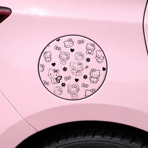 May include: A circular decal applied to a light pink car fuel door, featuring a repeating black line art pattern of Hello Kitty characters, small hearts, bows, and flowers. The design covers the entire surface of the round fuel cap cover.