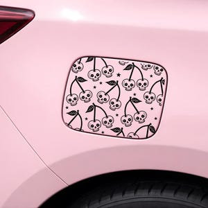 May include: A pink car with a black and white cherry skull design on the fuel filler flap. The design features cherries with skull faces, leaves, and stars. The car's tyre is visible at the bottom.