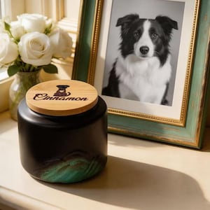 May include: A matte black ceramic jar with a bamboo lid featuring a laser-engraved dog silhouette and the name Cinnamon. The jar has a textured green accent at the base. The lid is circular and fits securely on top of the cylindrical container.