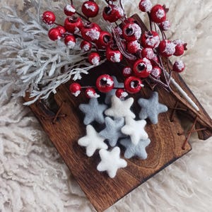 May include: A wooden tray with a white and gray felt star ornaments. The tray is decorated with a red berry sprig with white snow.