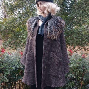 May include: A brown herringbone coat with a faux fur collar and large pockets. The coat has a button closure and is worn over a black dress. A dark scarf and hat complete the ensemble. The coat is displayed on a mannequin.